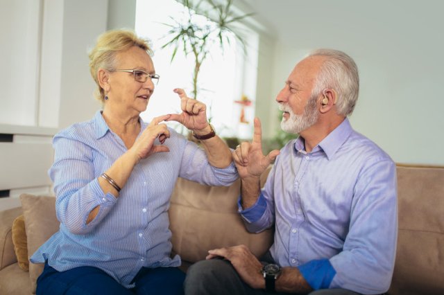Smiling senior woman talking using sign language with her hearing impairment man
