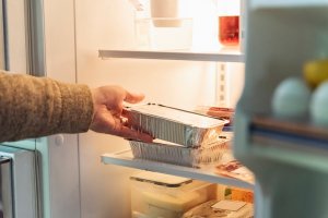 Man's hand taking takeout meal out of refrigerator.