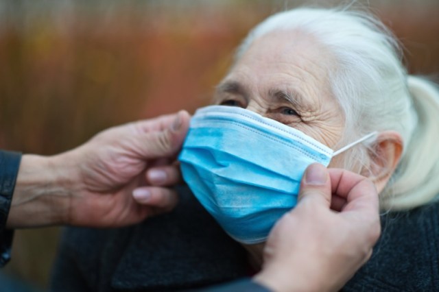 mans-hands-helping-a-senior-woman-to-put-on-protective-face-mask-picture-id1290309553