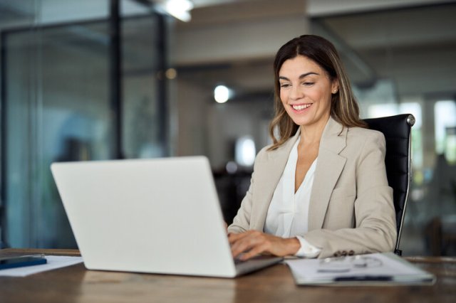 Happy mature professional business woman looking at laptop working in office.
