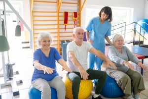 Group of senior people doing hands stretching exercises on pilates balls with therapist at rehab