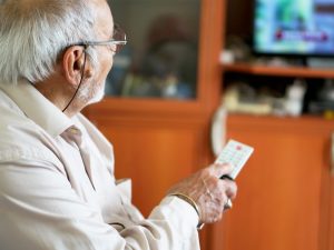 Senior man with TV remote control looks happy as he watches flat screen television