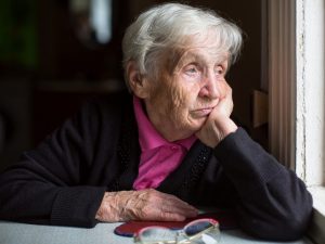 An elderly woman sadly looking out the window.